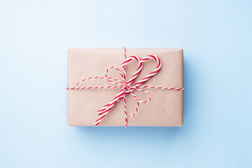 Christmas gift box wrapped in kraft paper with candy cane on blue background. Holiday card, top view.