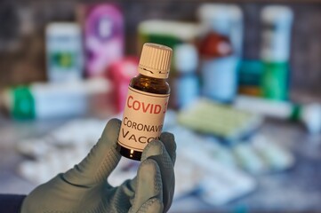Hand with blue glove holding a flask with vaccine. Coronavirus vaccine in a flask.