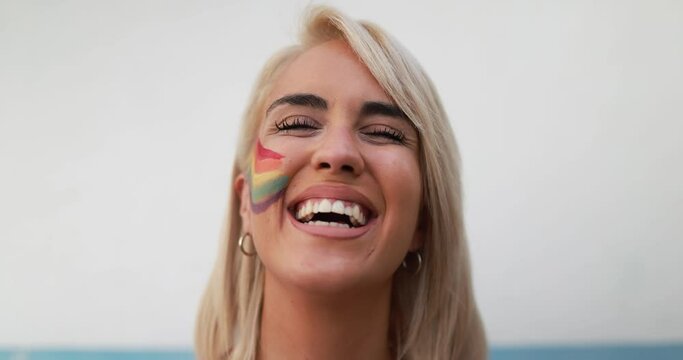 Blond girl with rainbow flag painted in her face smiling during gay pride protest