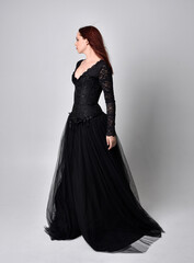 full length portrait of  woman wearing black gothic dress,  Standing pose  against a studio background.