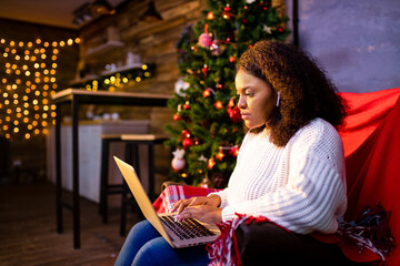 afro woman shopping online on laptop in cozy christmas interior.Preparing to xmas, bying on winter...