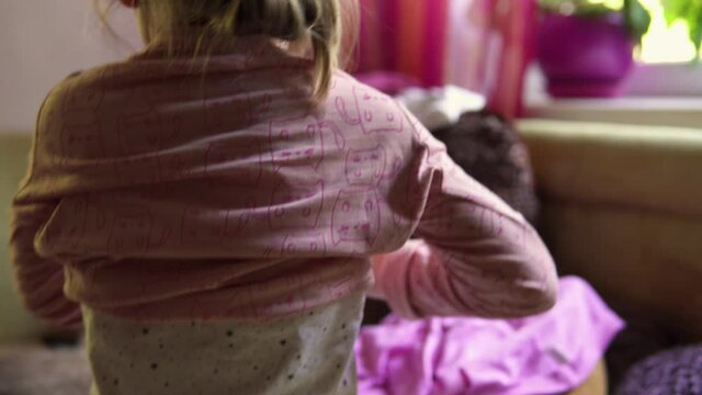 A little girl puts on a pink long sleeve t-shirt itself. Back view.