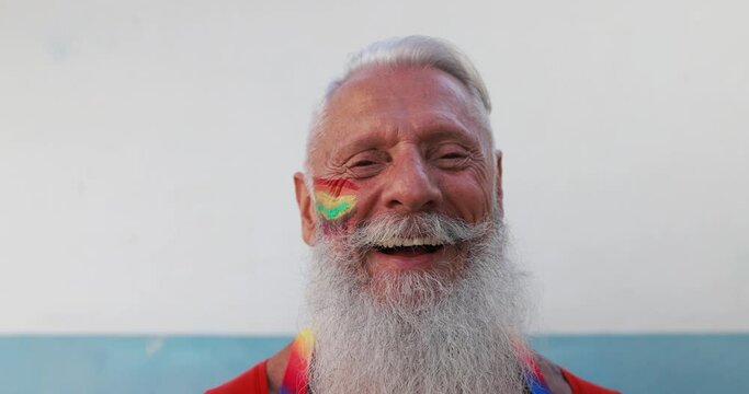 Senior gay man smiling in front of camera with rainbow colors painted on face - Slow Motion