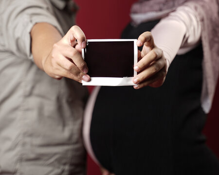 Pregnant woman holding ultrasound image. Cropped image of beautiful pregnant woman and her handsome husband hugging the tummy. Young pregnant woman holds her hands on her swollen belly. Love concept. 