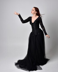 full length portrait of  woman wearing black gothic dress,  Standing pose  against a studio...