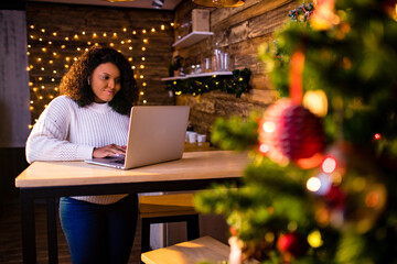 afro woman shopping online on laptop in cozy christmas interior.Preparing to xmas, bying on winter sales