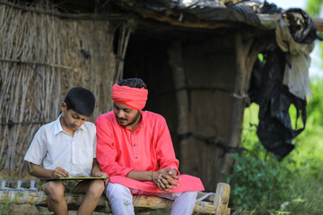 Cute indian farmer child studying with his father at home