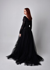 Naklejka premium full length portrait of woman wearing black gothic dress, Standing pose against a studio background.