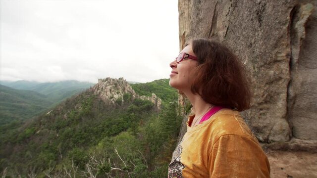 Portrait of young woman enjoying amazing landscape of mountains covered with evergreen forest. White City, Dragon Park in Russia