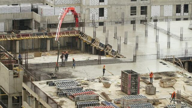 Workers at large construction site pour and level concrete. Modern monolithic industrial construction. Сonstruction industry