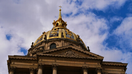 Closeup view of the golden colored majestic dome of historic Les Invalides cathedral in the center of Paris, France, grave of Napoleon Bonaparte on sunny day with blue sky and partly clouds.