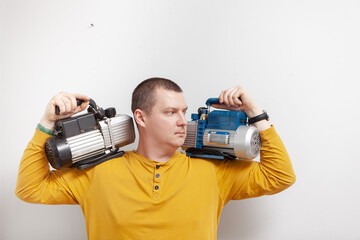 A strong man holds two vacuum pumps for refrigeration in his hands.