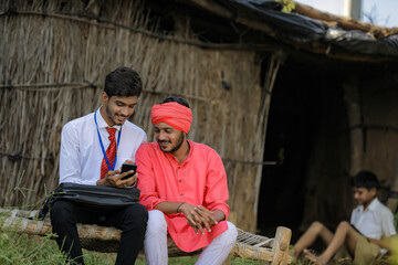Fototapeta na wymiar Young indian agronomist or banker showing some information to farmer in smart phone