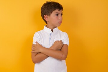 Image of upset Young handsome Caucasian little boy standing against yellow wall with arms crossed....