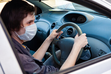 Fototapeta na wymiar Young man in protective medical mask driving a car. Person in a mask. Safety during coronavirus pandemic, epidemic covid-19. .