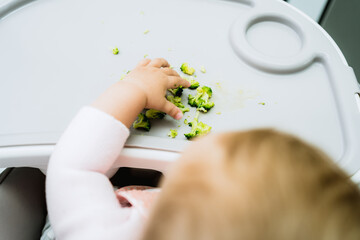 baby eating broccoli with hands in early stages of baby-led weaning