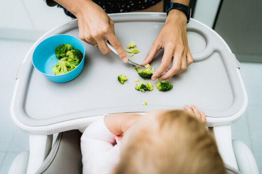 baby eating broccoli with hands in early stages of baby-led weaning at home