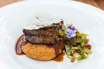 Tasty portion of meat cooked in its sauce on a bed of gratin mashed potatoes, accompanied by vegetables.