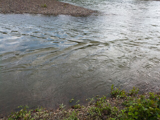 Detail from the river, a rapid stream of water flows through the gravel bed and creates waves on the surface of the water.