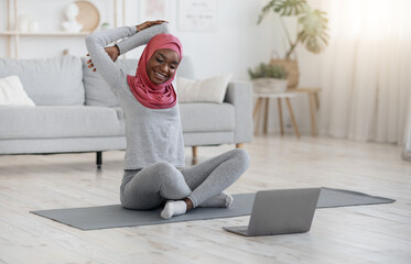 Healthy Lifestyle. Black Muslim Woman Doing Fitness Gymnastics With Laptop At Home