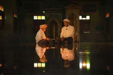 muslim boy sitting in mosque with islamic teacher learning koran book