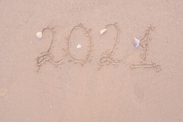 The concept of approaching New Year handwritten 2021, inscription. Numbers written on the sand shore with white shells, summer warm tropical beach holidays in 2021. Copy space. text on the sandy beach