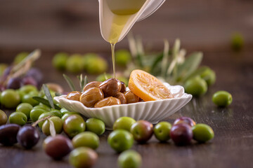 Green and black olives on the wooden floor and olive oil in a bottle and olive oil pouring from a white oil pot.