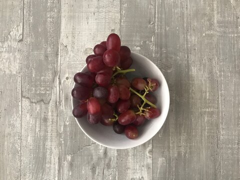 A Bowl Of Red Grapes Against A Wooden Background