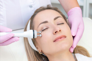 Hardware cosmetology. Close up picture of lovely young woman with closed eyes receiving rf lifting procedure in beauty salon.