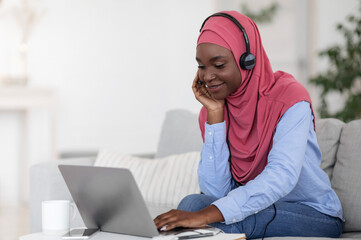 Positive black muslim lady watching webinar on laptop, studying at home