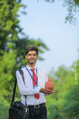 Young indian banker holding clay piggy bank in hand