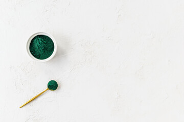 Green spirulina powder in a spoon and bowl on a white background. Horizontal orientation, copy space, top view.