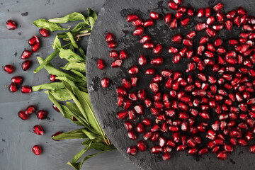 Scattered beautiful, juicy, ripe, red pomegranate seeds on a round stand of slate and pomegranate leaves on a black background