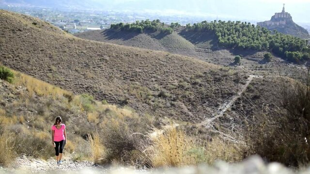 Woman hiking at mountain top in nature against cityscape of murcia and Monteagudo Christ in Spain