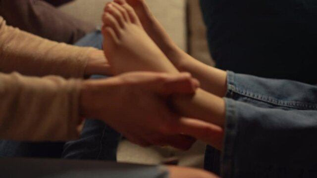Mother hands holding kid feet at home. Unknown parent arms playing kid legs.