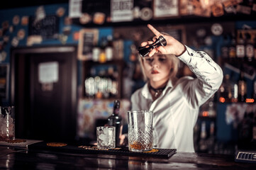 Professional woman bartending makes a show creating a cocktail behind bar