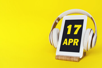 April 17th. Day 17 of month, Calendar date. Stylish headphones and modern tablet on yellow...