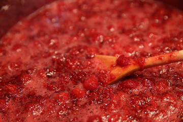 Cooking raspberry jam in a saucepan. Wooden spoon in a saucepan.