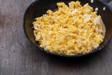 Scrambled eggs in an iron pan on the rustic wooden table