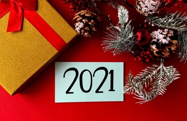 2021 on blue paper .Next to the gift box, fir branches, cones and red berries on a red...