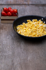 Scrambled eggs in an iron pan on the rustic wooden table