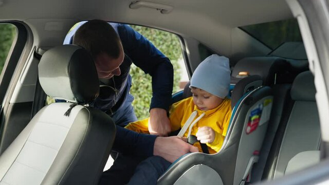 child safety in car, caring father puts his son in car seat and buckles seat belt during family trip