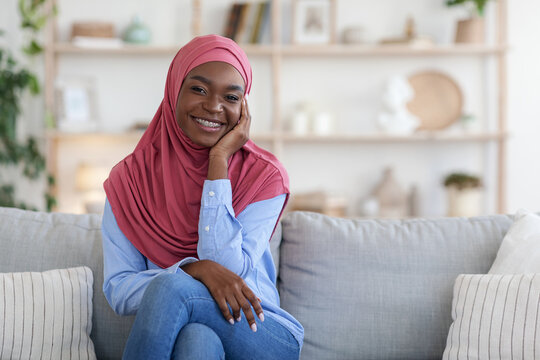 Modest Black Muslim Woman In Headscarf Relaxing On Couch At Home