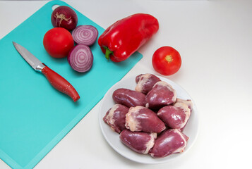 Fresh raw turkey hearts on a plate. Bird giblets ready for cooking with vegetables – paprika, tomato and red onion