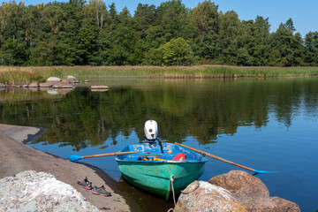 Boat with motor and oars moored to the shore on a forest lake
