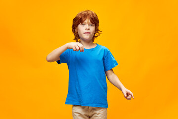 Red-haired child in a blue t-shirt gestures with his hands emotions yellow isolated background
