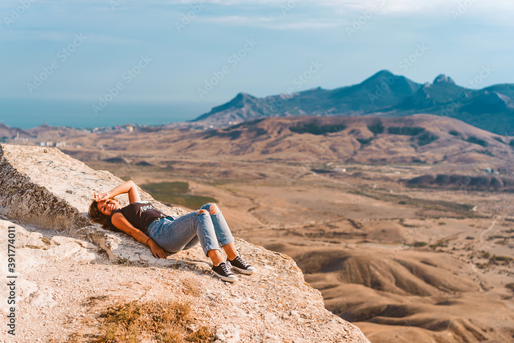 Wall mural a young beautiful woman with long hair and jeans lies on a rock in the koktebel valley in crimea. th