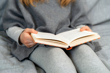 Caucasian girl with blond hair reading a book. Young teenager learning at home school in quarantine.