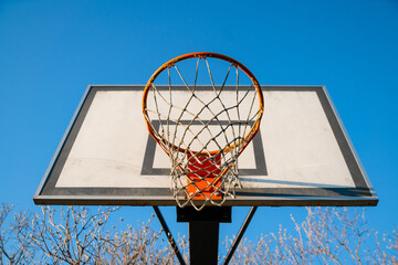 Naklejka premium Street basketball hoop on a sunny day with blue sky in the background. Urban youth game. Concept of success, scoring points and winning