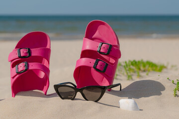 Pink sandals, sunglasses and sunscreen at the beach on a beautiful sunny day. Slippers in the sand...